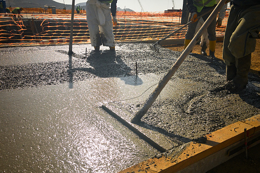 Construction workers use bull float to level, flatten and smooth concrete of cast in place foundation plate. Concrete leveling works with trowel at construction site
